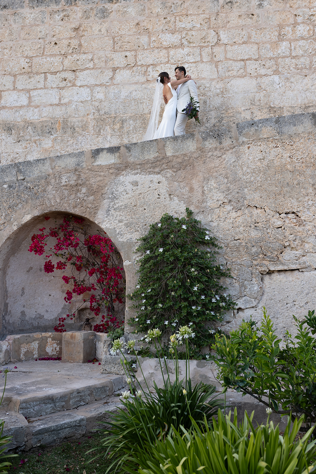 Wedding photo by Sus Pons of a bride and groom on a rustic stone staircase at a historic Menorcan venue, surrounded by Mediterranean garden
