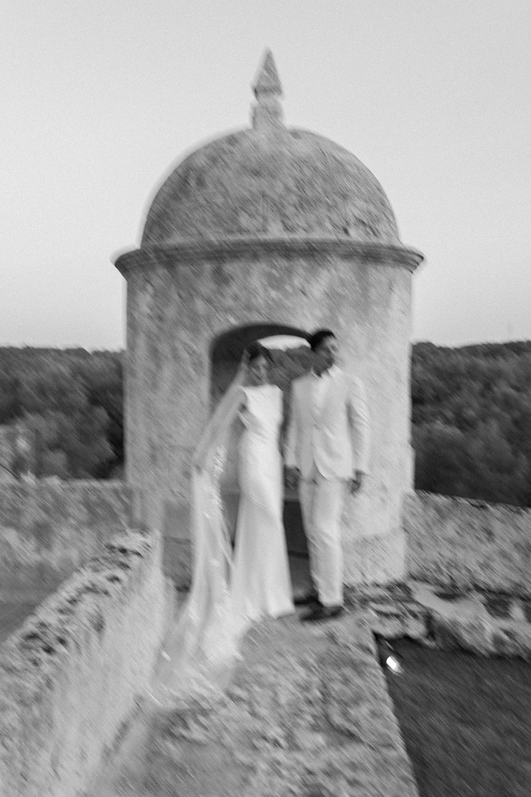 Bride and groom embracing on a stone staircase at a historic Menorcan venue, surrounded by Mediterranean garden and rustic architecture