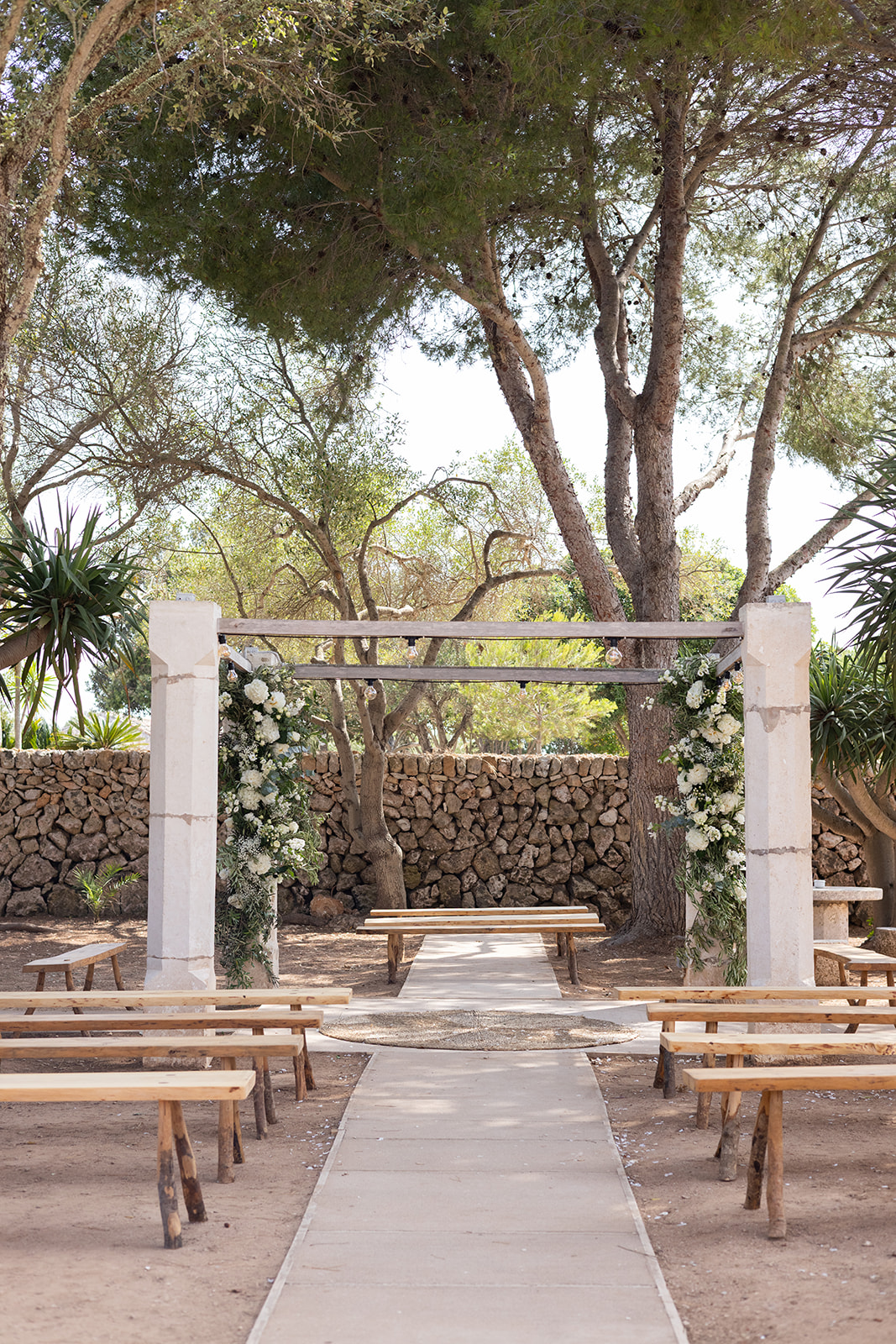 Rustic outdoor wedding ceremony setup with wooden benches and floral arch in a Menorcan finca, photographed by Sus Pons