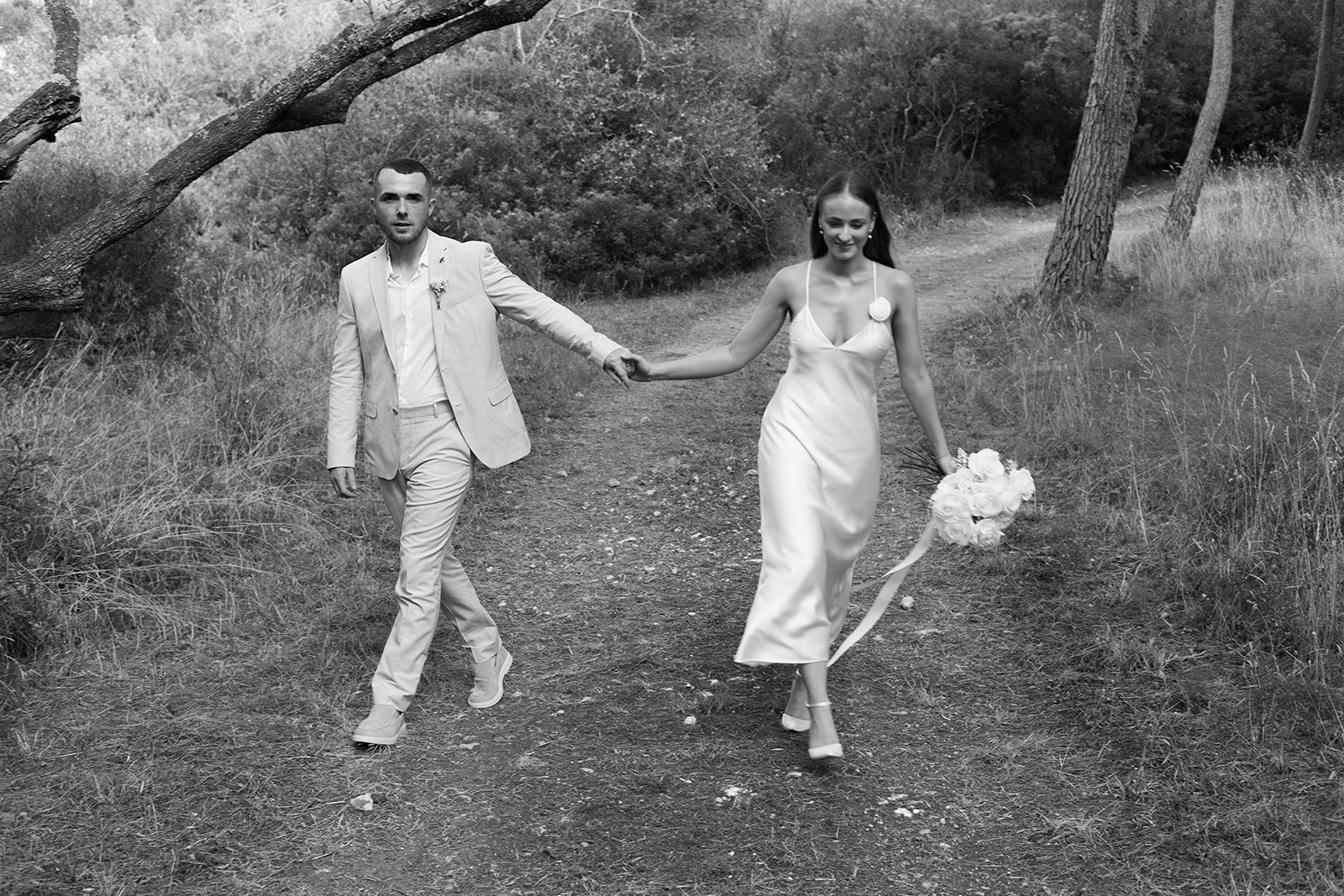 Bride and groom walking hand in hand through a forest path in Menorca, modern and elegant black and white wedding portrait by Sus Pons