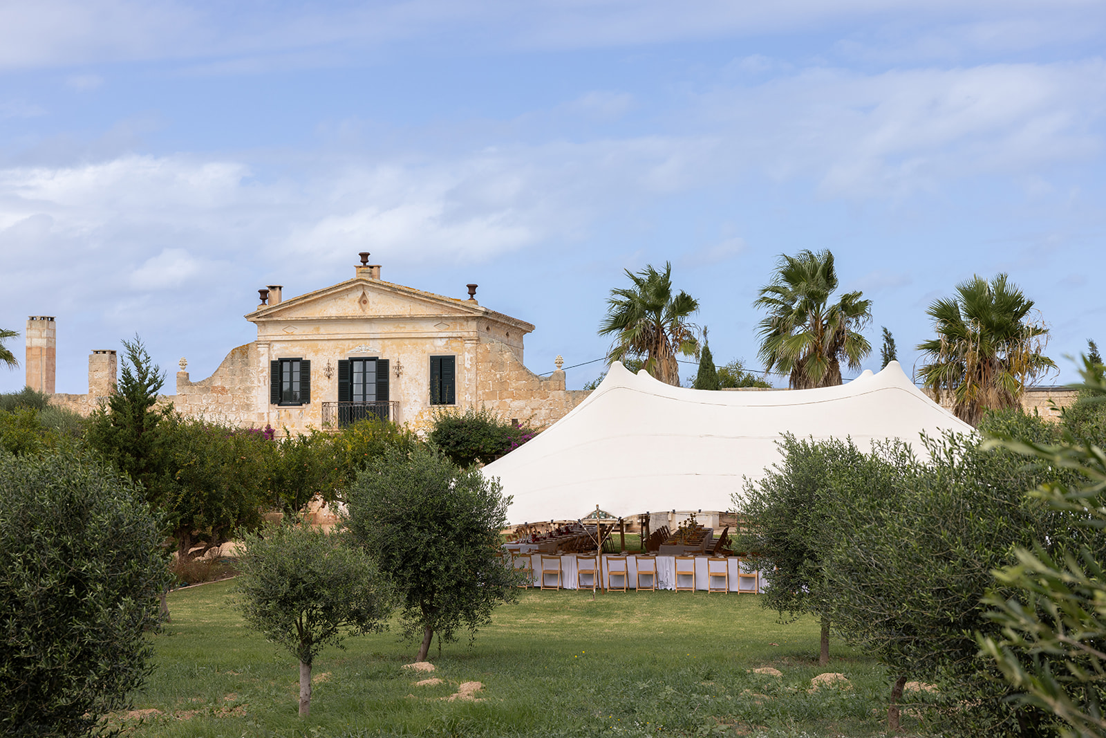 Wedding tent set up on the lawn of a traditional Menorcan finca with olive trees and Mediterranean architecture in the background